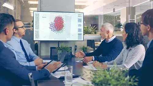 group of people sitting at a conference table looking at a chart on the screen