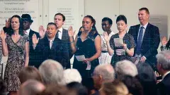 A diverse group of adults raise their right hands at a U.S. Naturalization Ceremony.