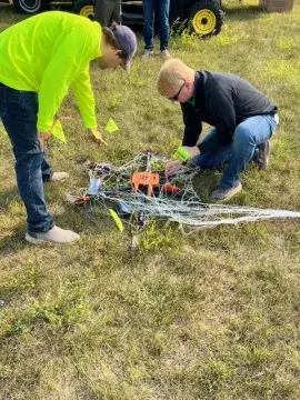 2 UND team members inspect and map out the drone debris on the field.