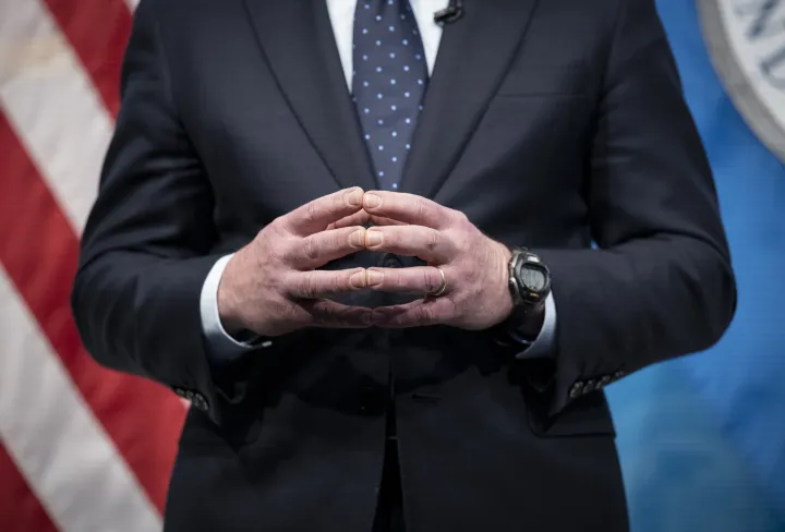 Image: Hands of a Suited Man in front of an American Flag Backdrop