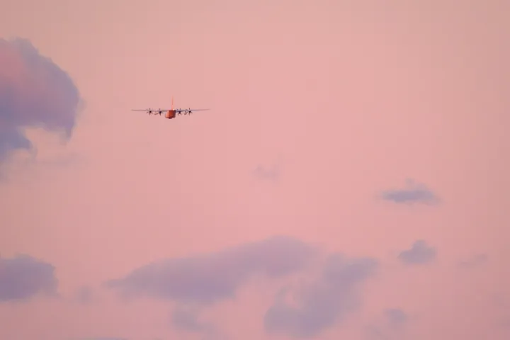 Image: A US Coast Guard (USCG) HC-130J aircraft flies during a sunset
