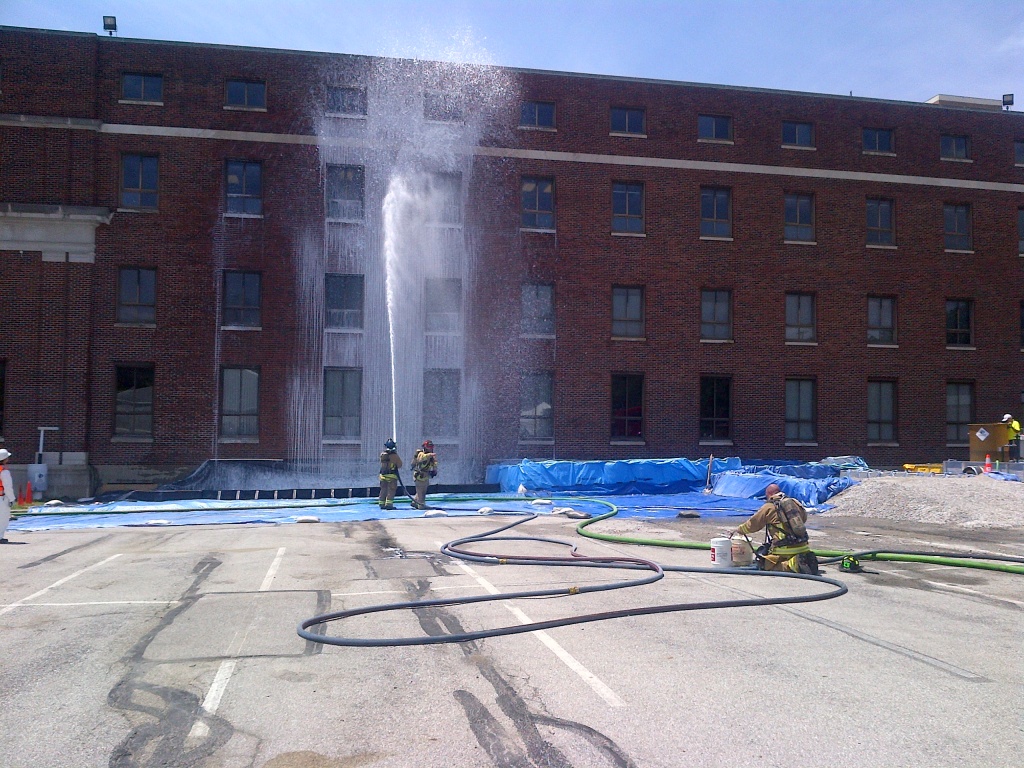 Firefighters spray decontaminating foam on a building