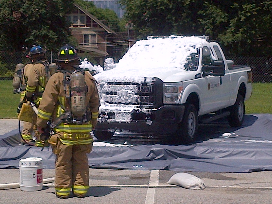 firefighters spray decontaminating foam on a white truck