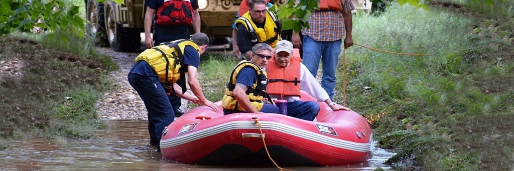 First Responder Shannon Buhl adn other responders sit in a red inflatable boat, being pushed into water.
