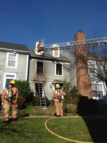 photo of firefighters on the ground and on a ladder in front of a house. 