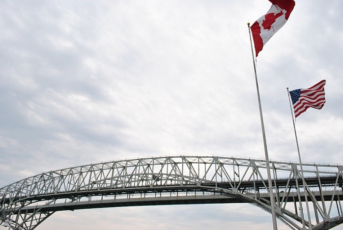 The United States of America flag, and Canadian flag, flys over a bridge.
