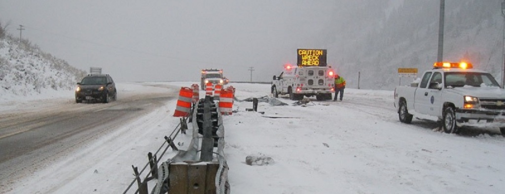 A highway covered in snow with a few emergency works and an emergency sign, "Caution Wreck Ahead"