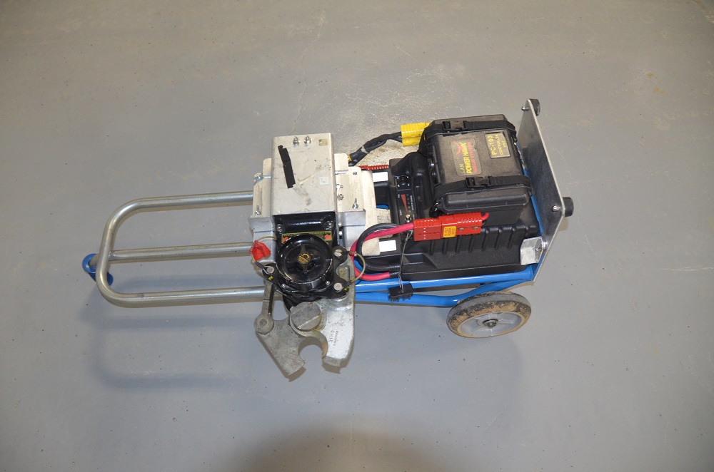 A standard 3-wheeled metal hand truck furniture dolly with a control unit box attached to the platform. Also attached is the metal Power Hawk tool, with scissor-like pincers.