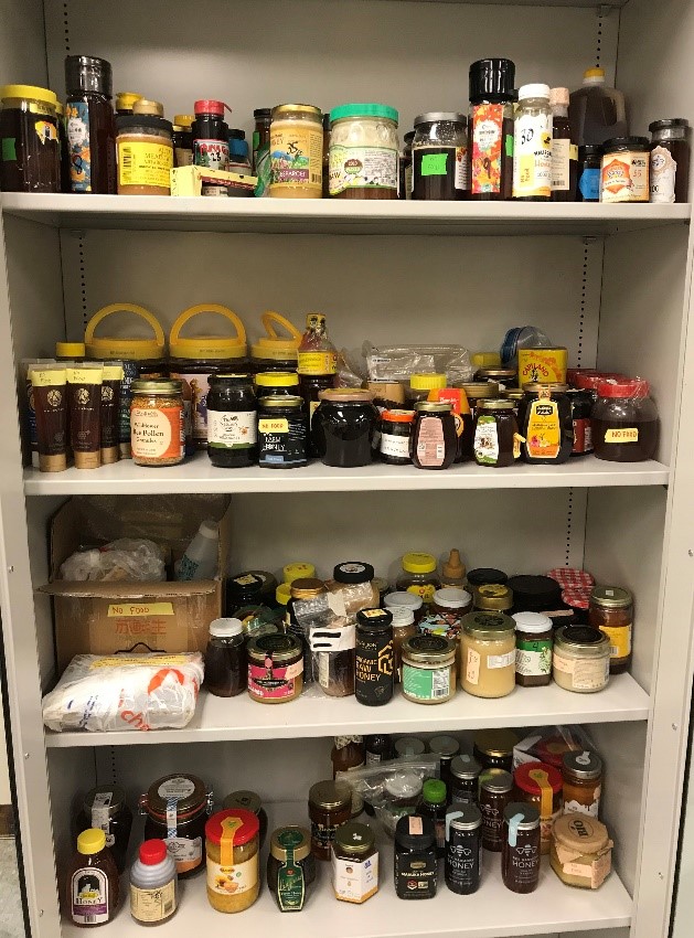 Variety of honey jars arranged in cabinet with four shelves.