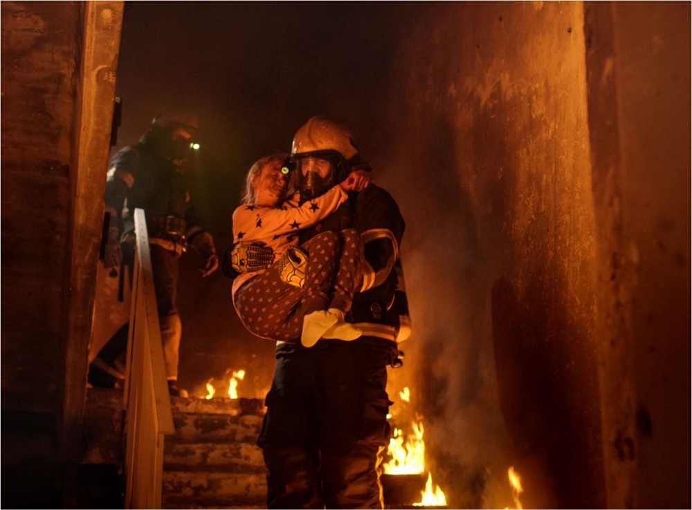 Firefighter carrying a child from a burning home. 