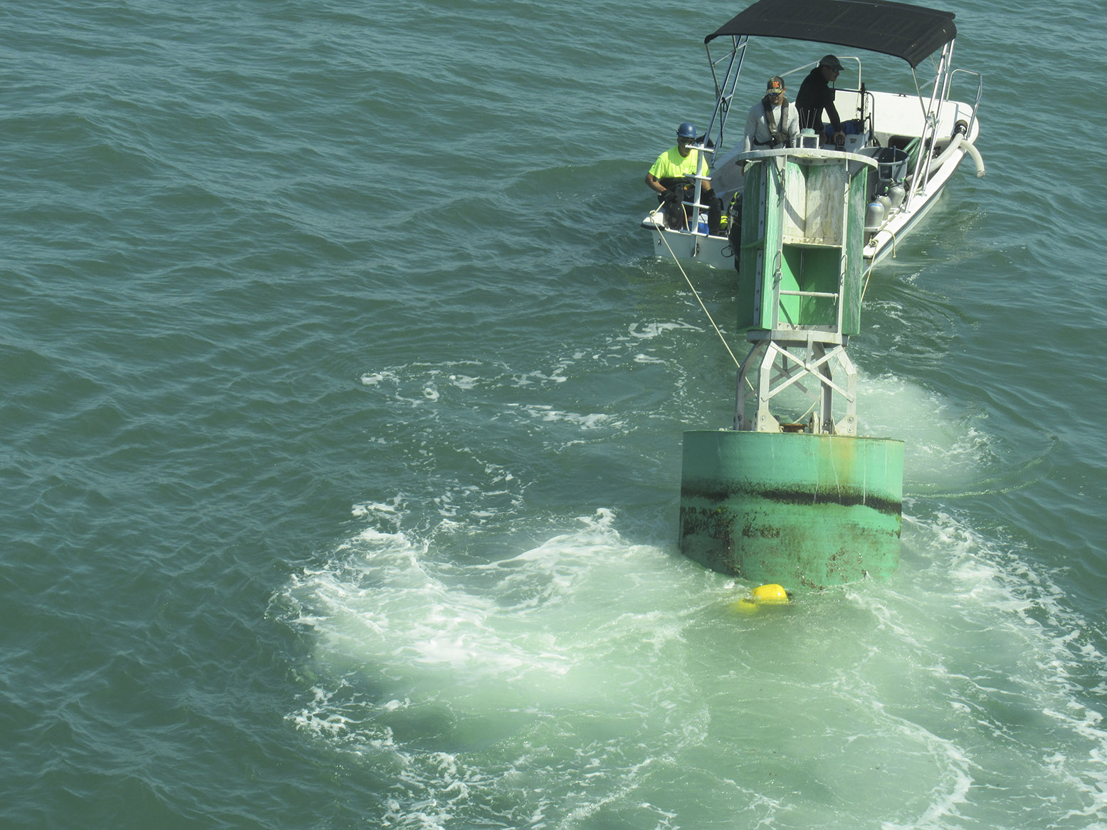 A diver boat tows a buoy with attached eco-mooring line toward divers awaiting to fasten it to one of the anchors. 