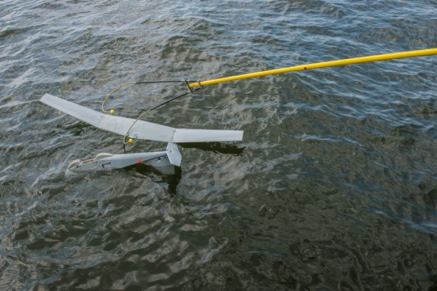 A drone floating in the water is recovered using a pole.