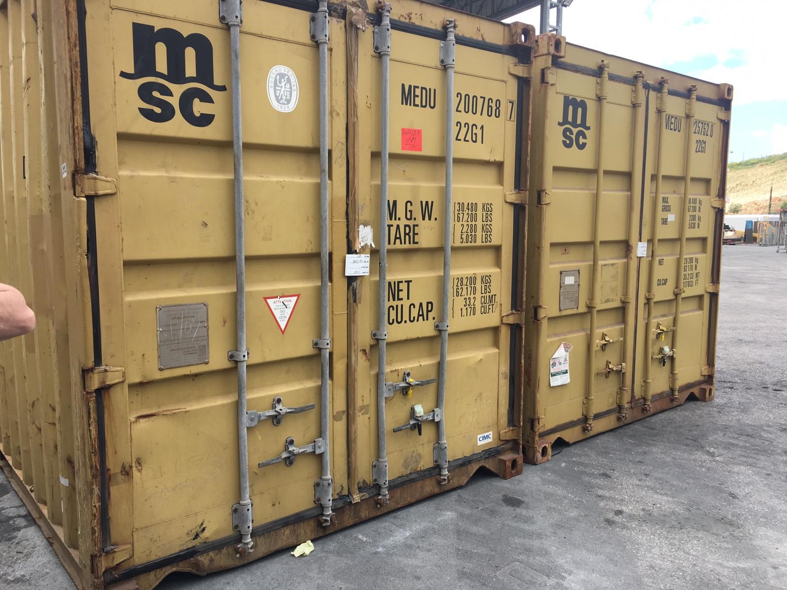 Two tan shipping containers are locked side-by-side on the concrete ground.
