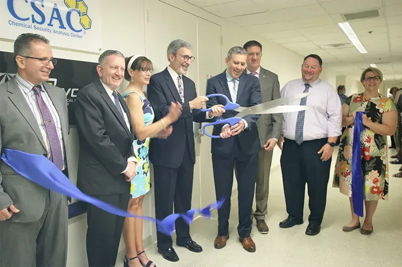 Chemical Security Analysis Center (CSAC) leadership happily wields giant scissors, cutting through a blue ribbon at the opening of CSAC’s new Chemical Security Laboratory.