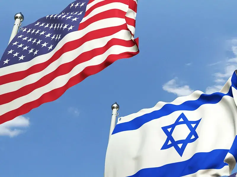 United States and Israeli flags flapping together in the breeze with blue sky in the background.