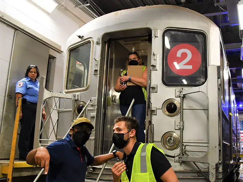 Evaluators confer with each other while standing behind a New York Metropolitan subway car within a subway tunnel.  