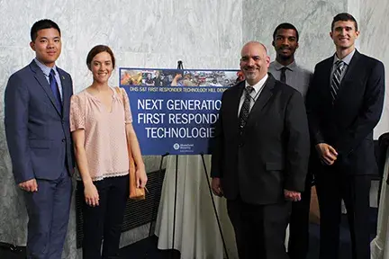 Bob Griffin and several other people standing in front of a Next Generation First Responder Technology event sign.