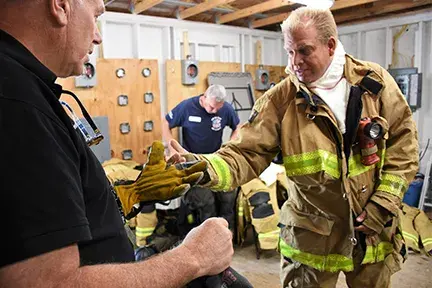 Three men in a room putting on firefighter gear.