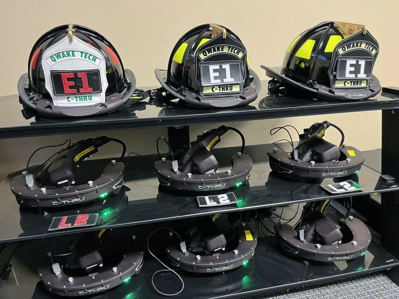 Firefighter helmets sit ready to be enhanced with C-THRU systems, charging on shelves below.
