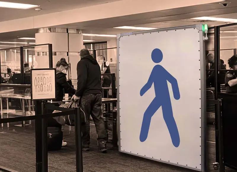 Image of a white passenger screening panel with a blue stick figure in a walking pose in the center setup in a busy airport checkpoint. Nearby are two passengers going through the airport security checkpoint.