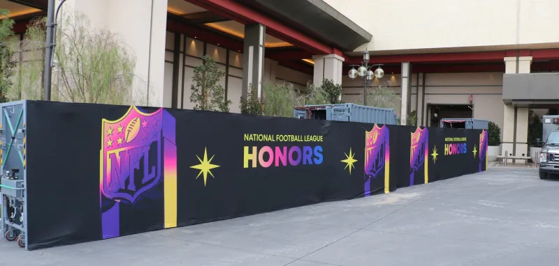 A RAPID barrier system approximately 40 feet in length in front of the entrance to a multi-story hotel complex. The barrier is covered with a fabric covered with designs and the text, “National Football League Honors.” 