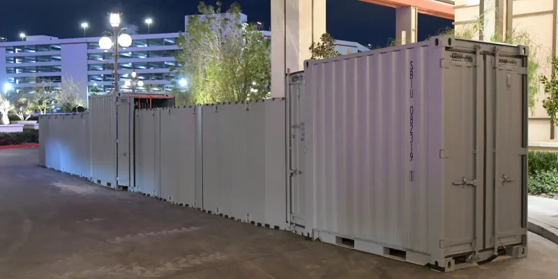Two connected sections of corrugated RAPID system metal barrier, about 30 feet in length, in front of the covered entrance of a hotel complex. There is a large parking structure in the background.