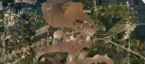 Satellite image depicts Houston, Texas, area after Hurricane Harvey in 2017. Brown water in the middle of the city image covers flooded areas of the city, showing the rivers overflowing into the city.