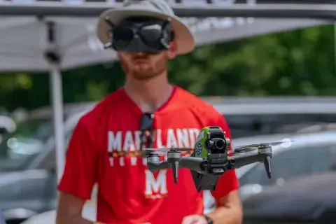 Close up of drone in flight with NIST Pathways Program participant and aeronautical engineering student Alex Fraley out of focus in the background.