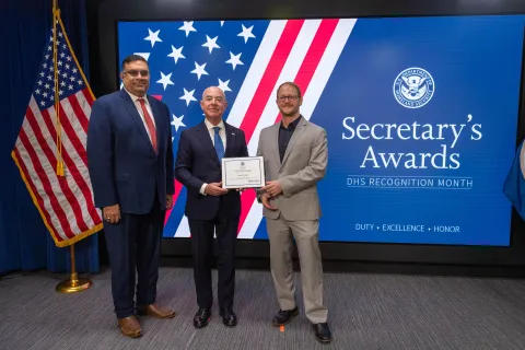 Left to Right: CISA Deputy Director Nitin Natarajan, DHS Secretary Alejandro Mayorkas, and Team Excellence Award recipient, Joshua Finney.