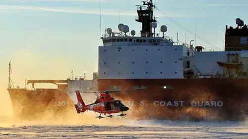 Coast Guard helicopter hovering above water next to Coast Guard ship