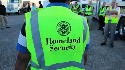 Person standing with their back to the camera, facing a group of evaluators, with U.S. Department of Homeland Security seal, Homeland Security, displayed on a safety vest.