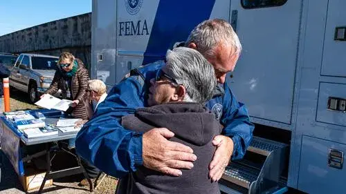 Two people hugging next to FEMA vehicle