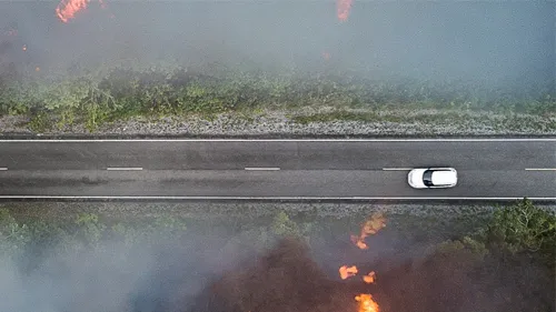 car driving on road with wildefires on either side