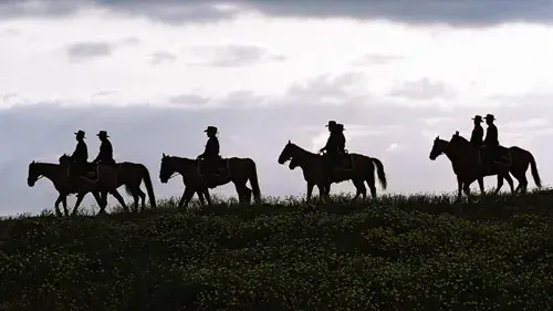 Image of several U.S. Border Patrol officers on horses riding across a ridge.