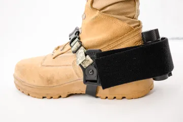 A desert tan combat boot with the WarLoc tracking device attached to it. The device is positioned at the back of the heel and held in place with large black straps. 