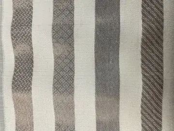 A closeup of off-white fabric with dark beige stripes, each with a different geometric pattern.