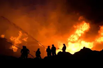 At night, several firefighters are on a ridge battling an enormous blaze.