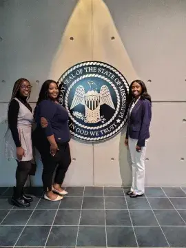 Dr. Murphy (right) and two student researchers posing next to a Mississippi state seal.