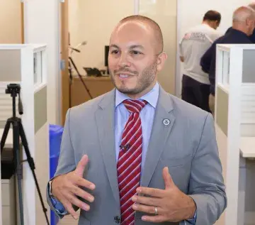A man in suit standing between cubicle office spaces giving an interview.