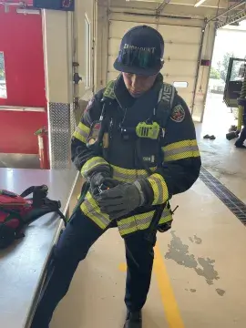 A Fairmount firefighter in full protective gear (jacket, gloves, pants, boots, and equipment) operates a wearable chemical sensor badge during an operational field assessment, to see how well it would work in the field. 