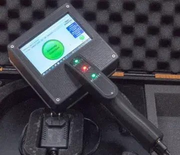 Closeup of the handheld screening wand device. Screen reads “Anomaly Detection” and handle has lights with labels, “Detect, Scan, and BG/PEF” under each light.