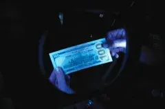 A person inspecting a 100 dollar bill underneath a blacklight
