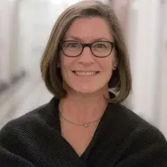 Photograph of Dana Chisnell, a woman with chin-length light brown hair, and glasses. She is wearing a black shirt and in front of a light-colored backdrop.