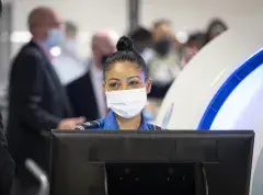 A headshot picturing a TSA agent wearing a surgical mask. She has her hair up in a bun on top of her head.