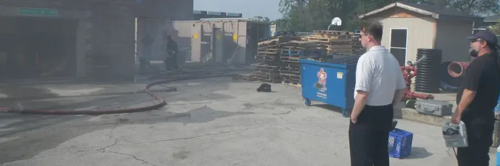 josh dennis and a fellow responder look at building with a fire hose in front of it and wooden pallets to the side.
