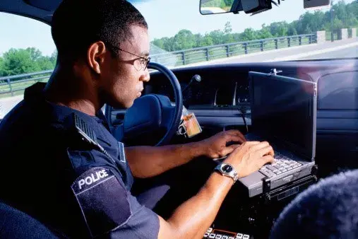 A police officer sits in his car typing on a laptop