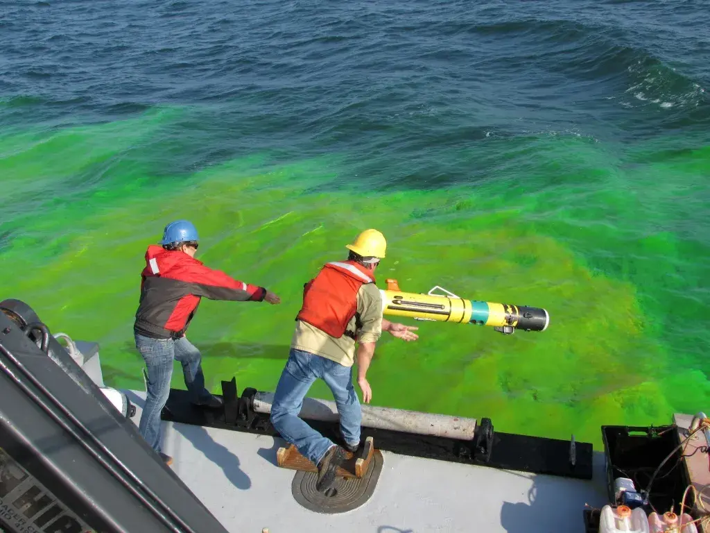 Two men throw the LRAUV off a ship into Arctic waters that have been dyed.